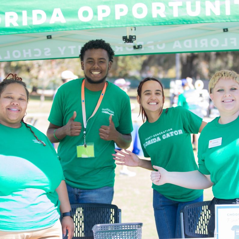 A group of four students smile at the camera under a green canopy.