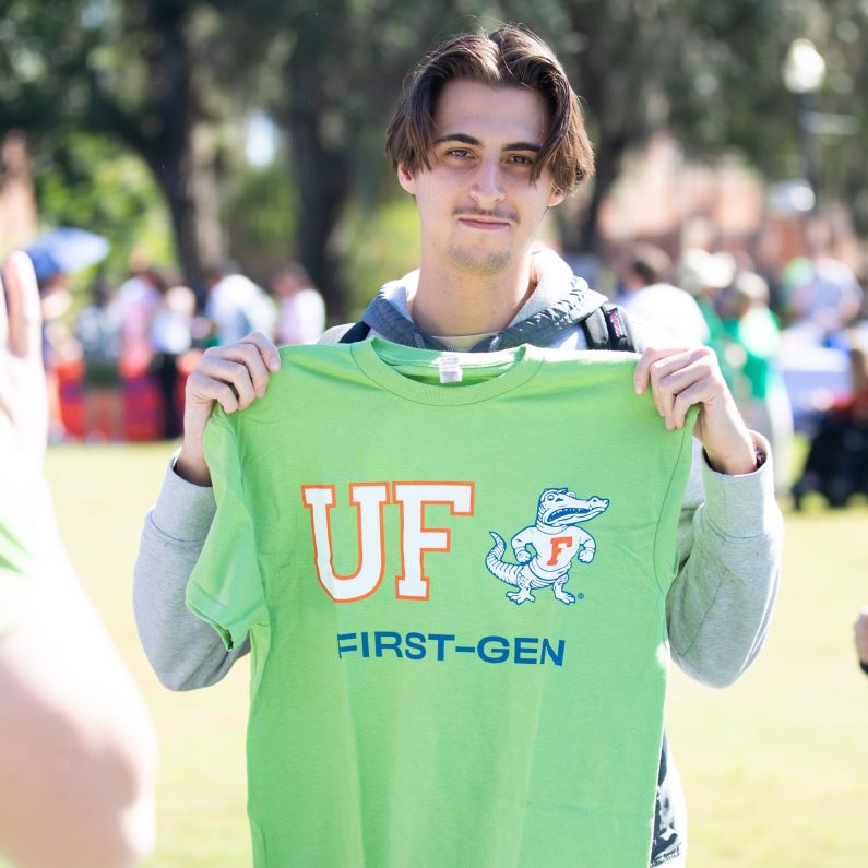 Student holding a green t-shirt that features the UF logo, fighting gator, and "#First-Gen".