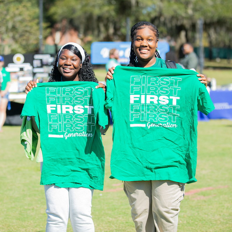 Two students hold up green "First Generation" t-shirts.