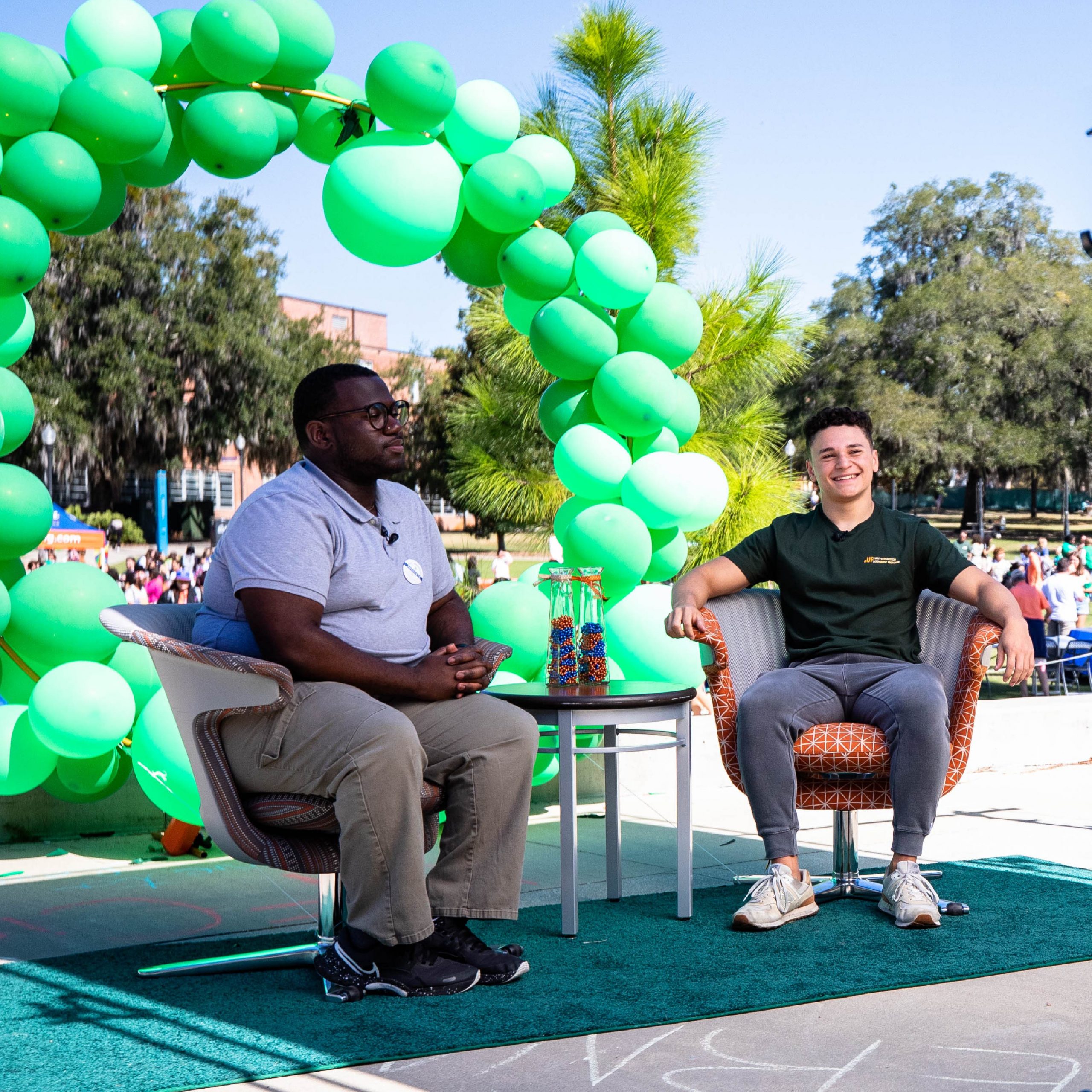 Student doing an interview in front of a green balloon arch.