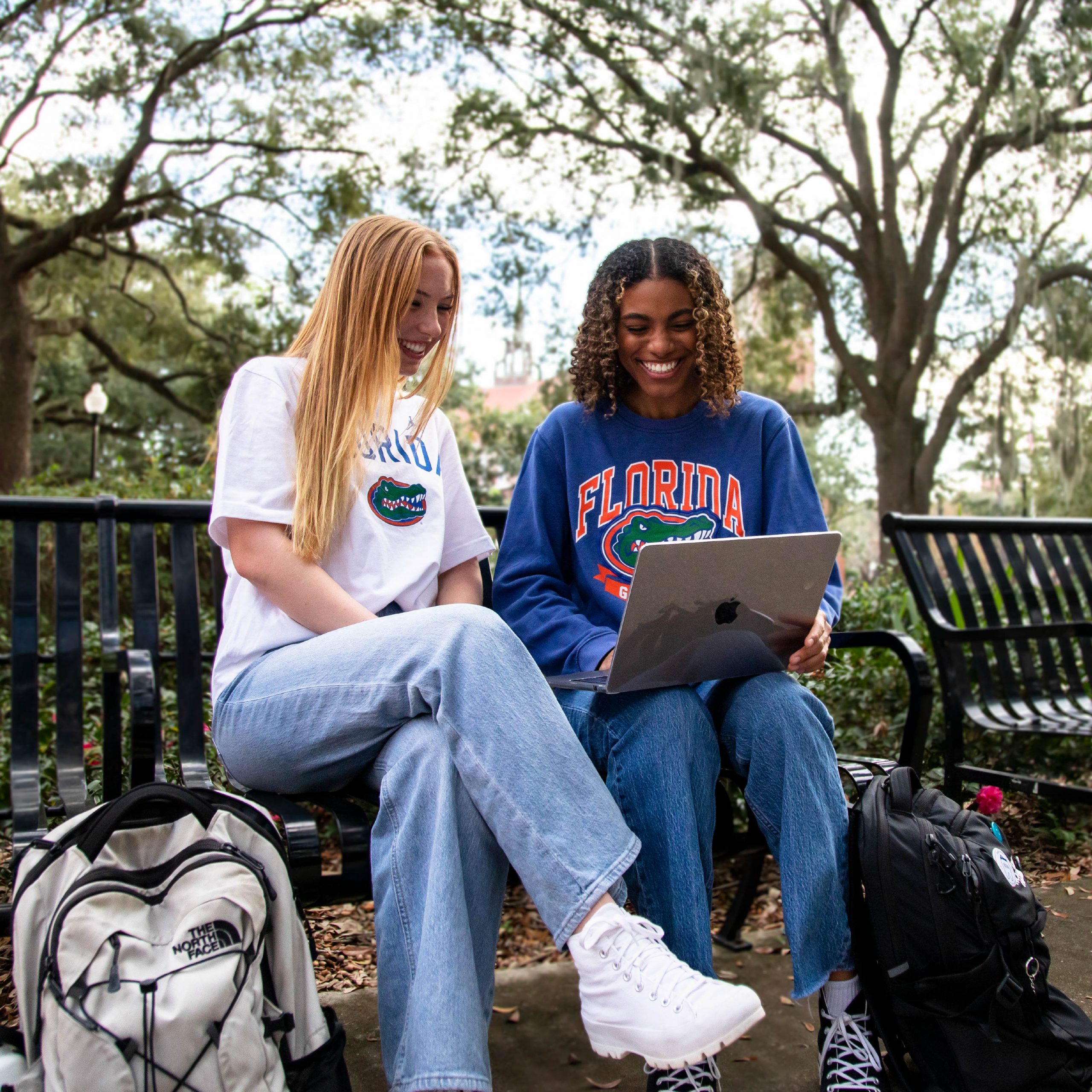 Two students sitting on a bench outside working on a computer.
