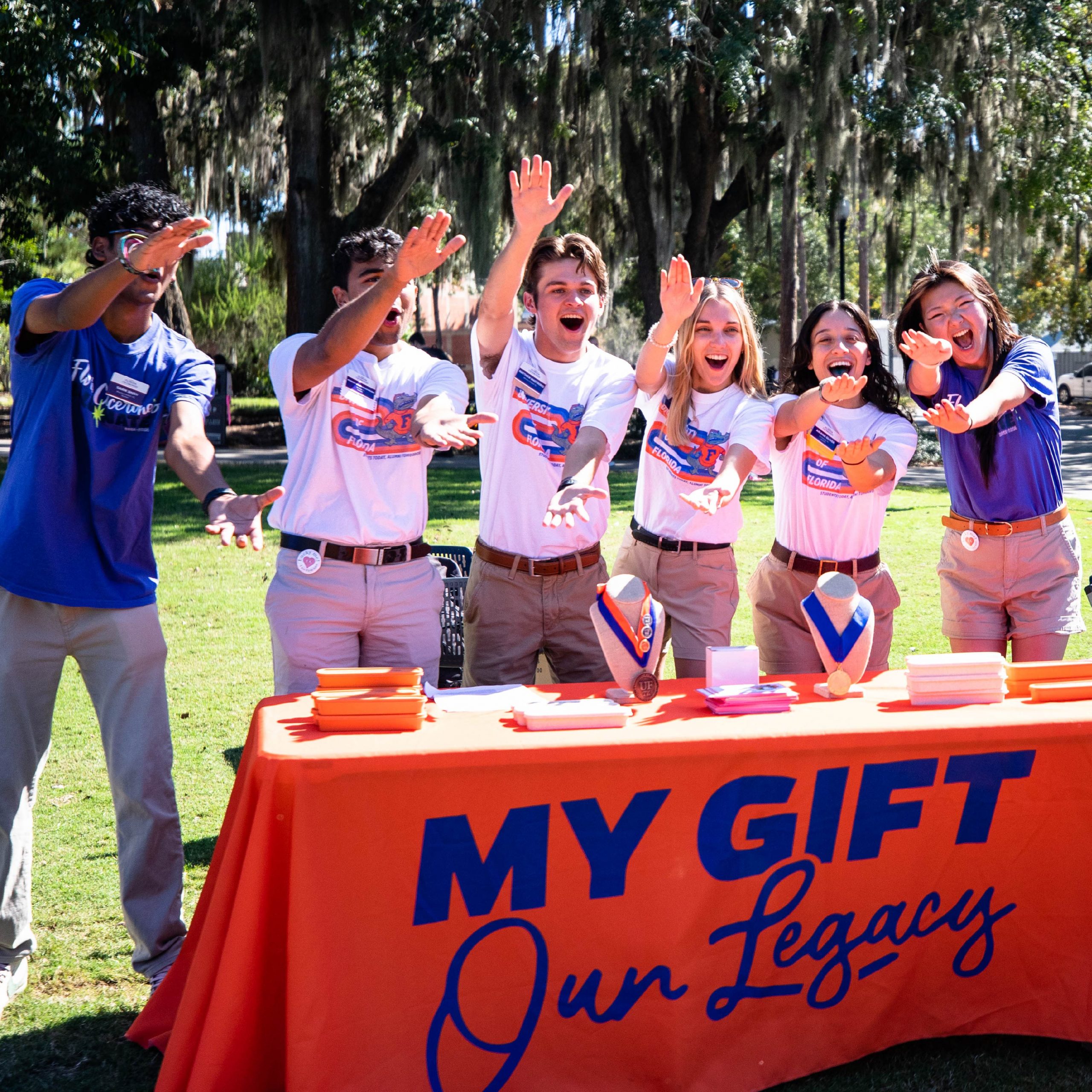 A group of students do the gator chomp behind a table.
