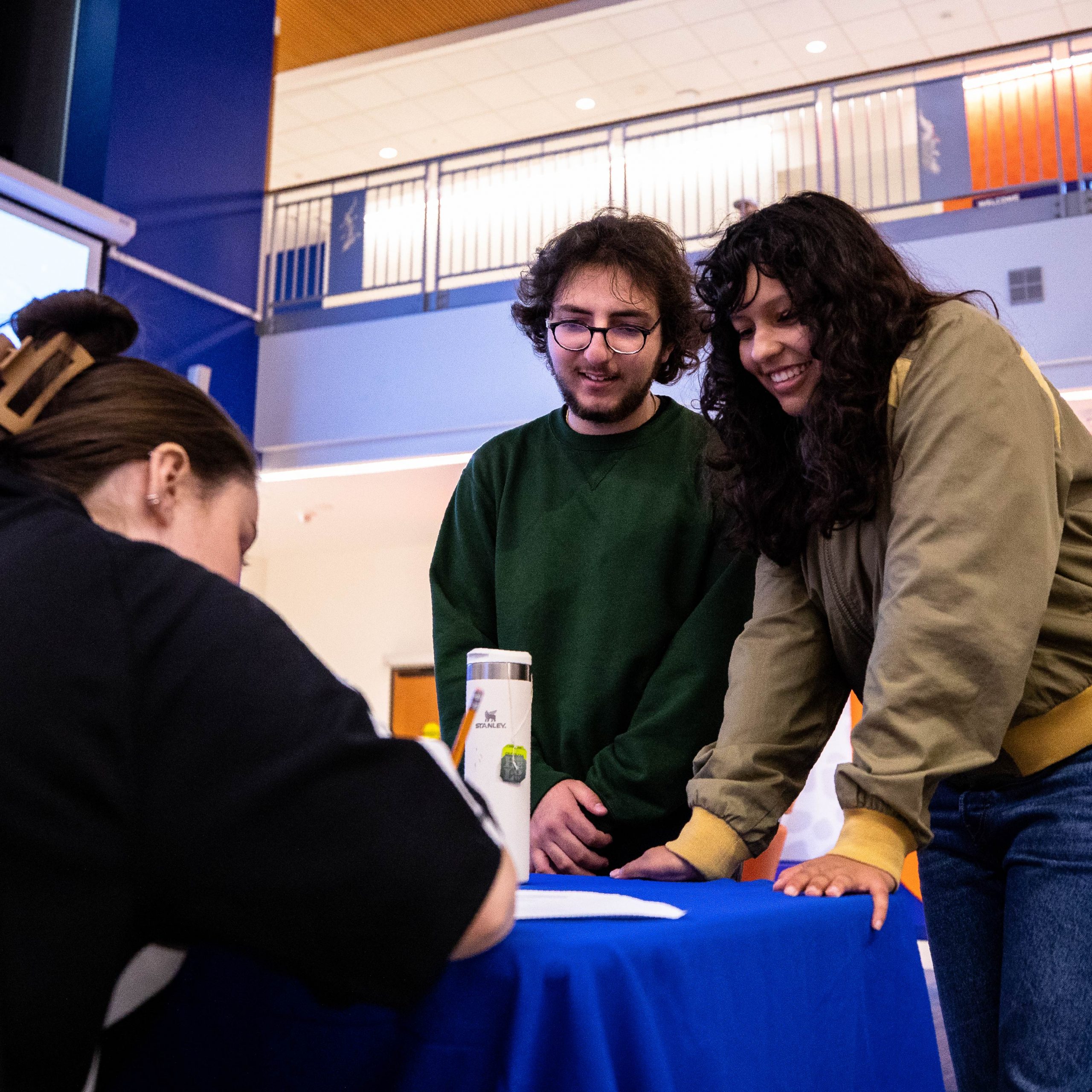 Two students connect with a staff member at a information table.