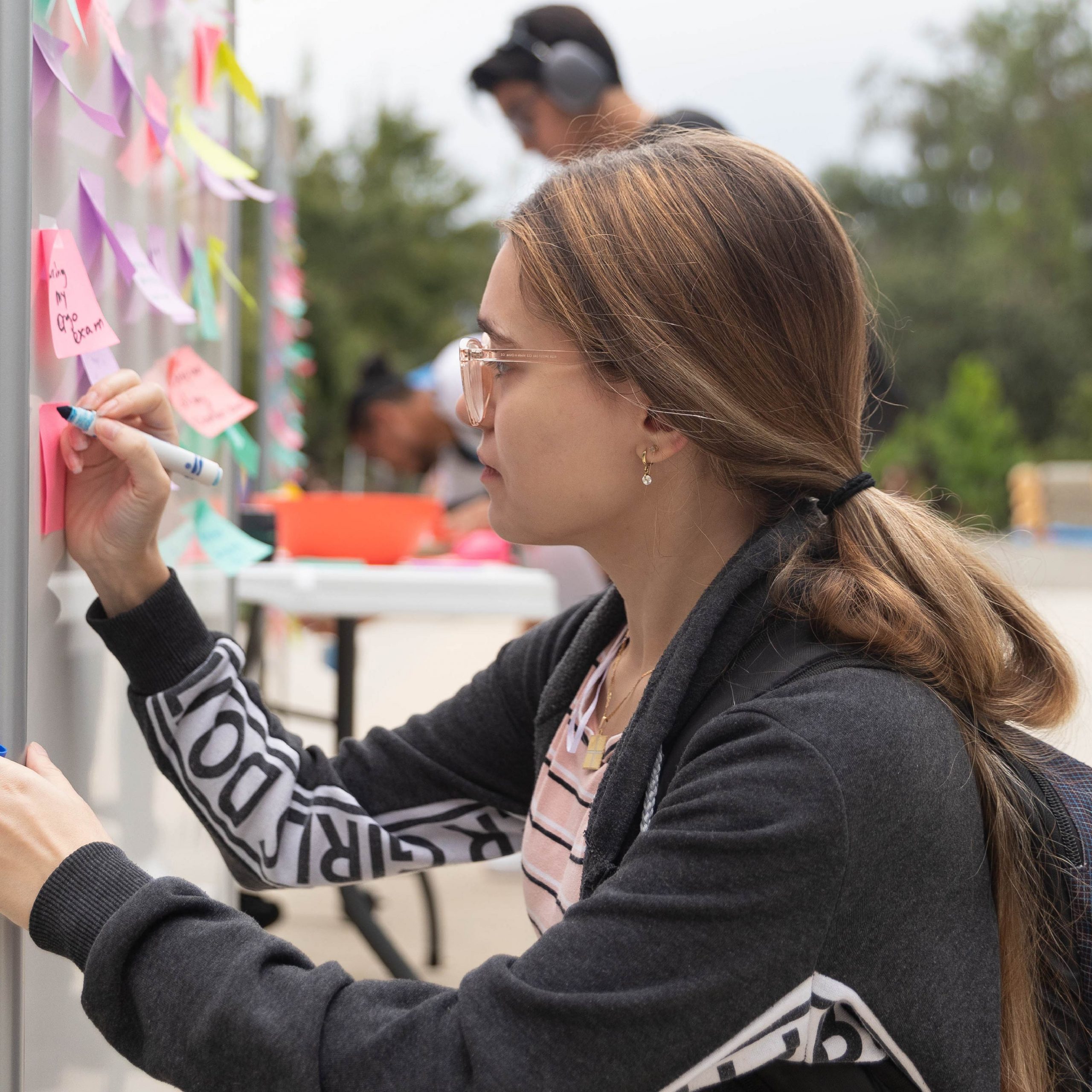 A student writing an encouraging message on a white board outside.